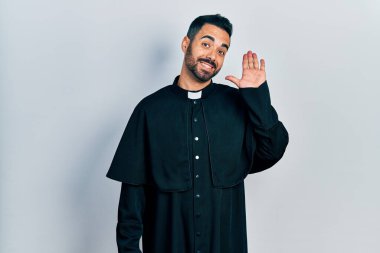 Yakışıklı, sakallı, Katolik rahip cüppeli, mutlu ve güler yüzlü, dostça bir jest yapan bir adam. 