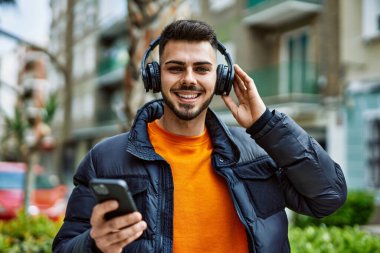 Yakışıklı, sakallı, neşeli, kendine güvenen, kışlık palto giyen, akıllı telefondan müzik dinleyen bir İspanyol.