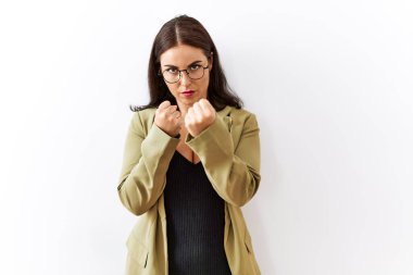 Genç esmer kadın izole edilmiş arka planda duruyor. Yumruk savunma hareketleriyle dövüşmeye hazır. Kızgın ve üzgün bir yüz, sorundan korkuyor. 