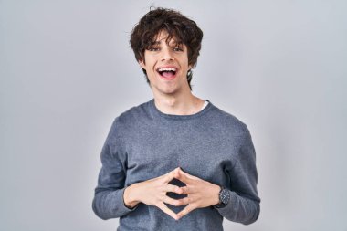 İzole edilmiş arka planda duran genç adam ellerini birleştirip gülümseyerek gevşemiş ve neşeli olmasını diliyordu. Başarı ve iyimserlik 