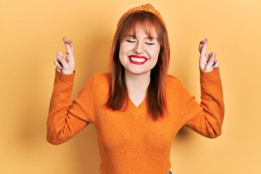 Kızıl saçlı, turuncu süveter giyen genç bir kadın umut ve gözlerin kapalı bir şekilde gülümseyerek işaret ediyor. Şans ve batıl inançlar. 