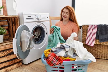 Çamaşır odasında çamaşır makinesiyle çamaşırları temizleyen genç kızıl saçlı kadın.