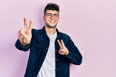 Gündelik kıyafetler ve gözlük takan genç İspanyol adam kameraya bakıp zafer işareti yapıyor. İki numara.. 