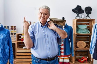 Perakende dükkanında elinde alışveriş poşetleri olan yaşlı bir adam mutlu bir şekilde elini ve parmağını kenarı işaret ediyor. 