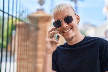 Genç beyaz adam gülümsüyor. Kendine güveniyor. Akıllı telefondan konuşuyor.