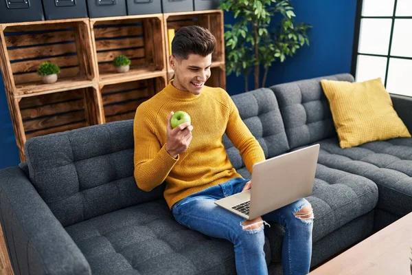 Young Hispanic Man Using Laptop Eating Apple Home —  Fotos de Stock