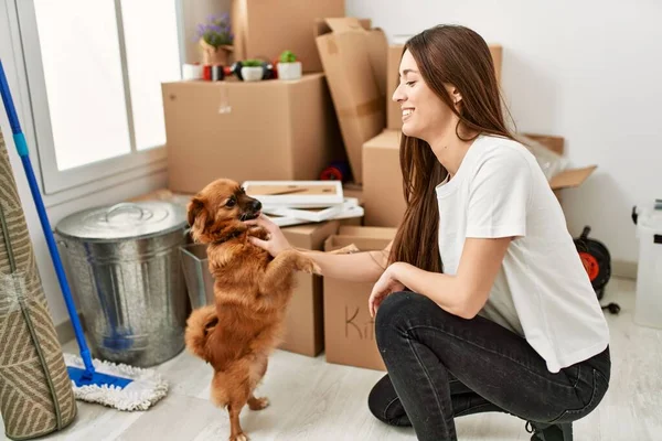 Young hispanic woman smiling confident playing with dog at new home