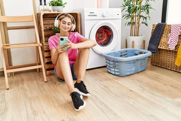 Jonge Blanke Vrouw Met Behulp Van Smartphone Koptelefoon Wachten Wasmachine — Stockfoto