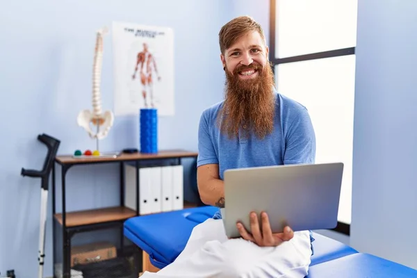 Young Redhead Man Wearing Physiotherapist Uniform Using Laptop Physiotherapy Clinic — 图库照片
