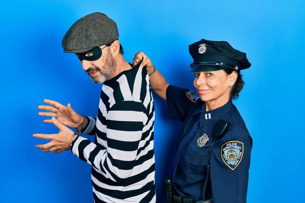 Middle age couple of hispanic woman and man wearing thief and police uniform looking to side, relax profile pose with natural face and confident smile.