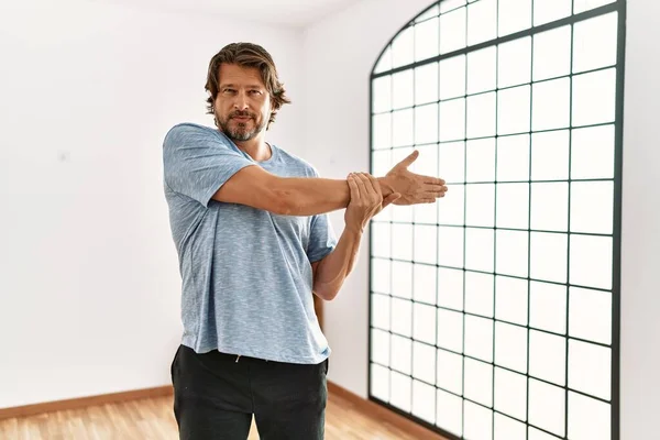 Middle age caucasian man stretching at sport center