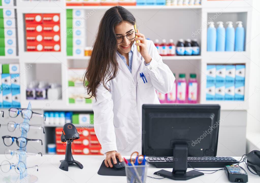 Young hispanic girl pharmacist talking on the smartphone working at pharmacy