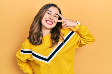 Gündelik kıyafetler giyen genç İspanyol kız barış sembolü yapıyor. Yüzünde parmaklar, gülümseyerek zaferi gösteriyor. 