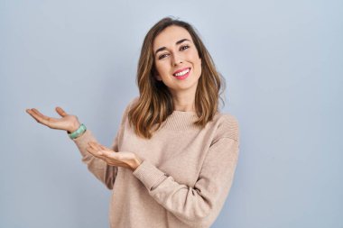 Young woman standing over isolated background inviting to enter smiling natural with open hand 
