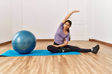 Genç Latin kadın spor merkezinde formda top kullanarak esniyor.