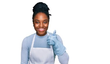 Önlük takan, mutlu ve pozitif gülümseyen genç Afrikalı Amerikalı kadın, başparmağıyla mükemmel ve onay işareti yapıyor. 