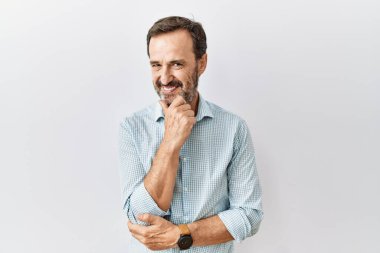 Orta yaşlı, sakallı bir adam izole edilmiş arka planda duruyor. Kameraya bakıyor. Kollarını kavuşturup, çenesini kaldırarak gülümsüyor. Olumlu düşünmek. 