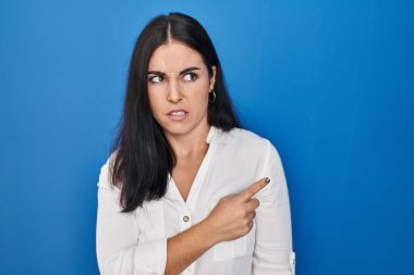 Mavi arka planda dikilen genç İspanyol kadın endişeli ve endişeli bir ifadeye işaret ediyor. 