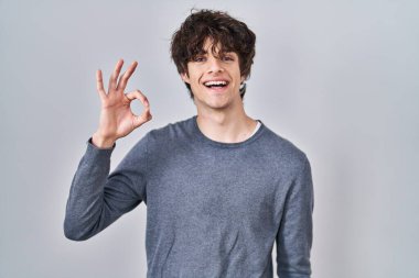 İzole edilmiş arka planda duran genç adam gülümsüyor ve el ve parmaklarıyla 