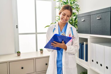 Doktor üniforması giyen genç İspanyol kadın klinikte sağlık raporu yazıyor.