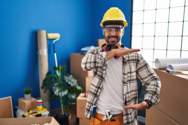 Sakallı, ev tadilatında çalışan, elleri büyük ve büyük bir işaret gösteren, ölçü sembolü olan genç İspanyol bir adam. Kameraya bakıp gülümsüyor. ölçüm kavramı. 