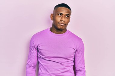 Genç siyah bir adam pembe bir süveter giyiyor gülümsüyor yan tarafa bakıyor ve düşünüyor.. 