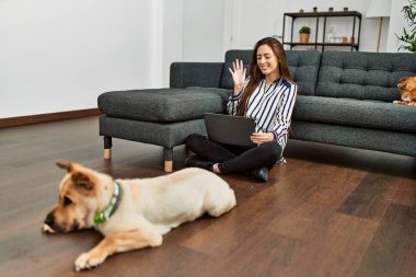 Genç İspanyol kadın evde köpeklerle yerde otururken görüntülü konuşma yapıyor.