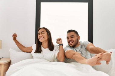 Genç latin çift, esniyor ve kollarını uzatıyor yatağa oturuyorlar..