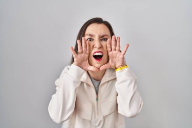 Middle age hispanic woman standing over isolated background shouting angry out loud with hands over mouth 