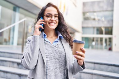 Genç İspanyol kadın yönetici kahve içiyor ve caddede akıllı telefondan konuşuyor.
