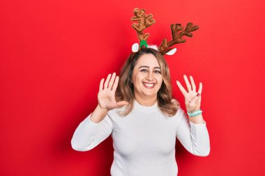 Orta yaşlı beyaz kadın şirin Noel geyiği boynuzları takıyor dokuz numaralı parmaklarını gösterip gösterirken kendinden emin ve mutlu gülümsüyor.. 