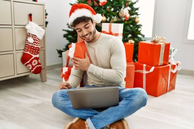 Genç İspanyol adam mutlu bir şekilde gülümsüyor. Evde dizüstü bilgisayar kullanıyor..