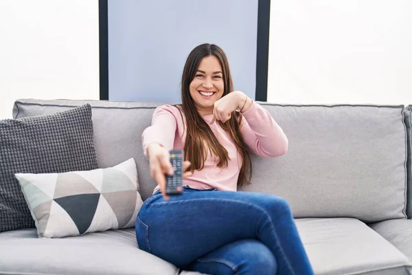 Jovem Morena Segurando Televisão Controle Remoto Apontando Dedo Para Auto — Fotografia de Stock