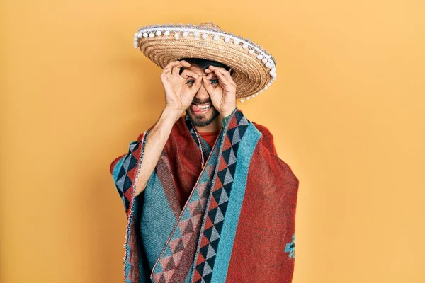 Homem Hispânico Jovem Segurando Chapéu Mexicano Fazendo Gesto Como Binóculos — Fotografia de Stock