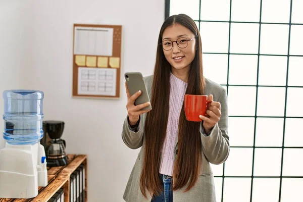 Νεαρή Κινέζα Επιχειρηματίας Χρησιμοποιώντας Smartphone Και Πίνοντας Καφέ Στο Γραφείο — Φωτογραφία Αρχείου