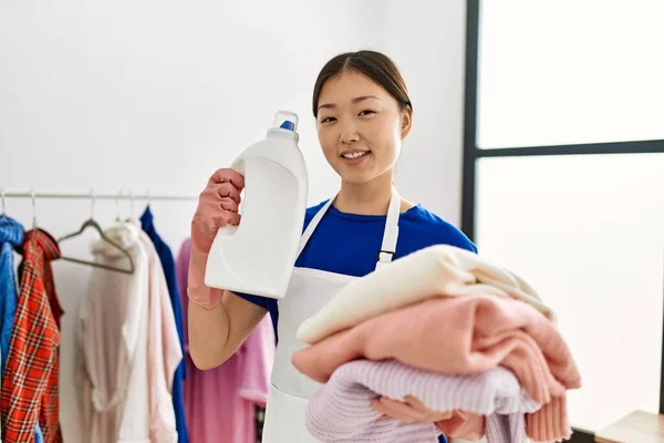 若い中国の主婦は家で折り畳まれた服や洗剤ボトルを保持 — ストック写真