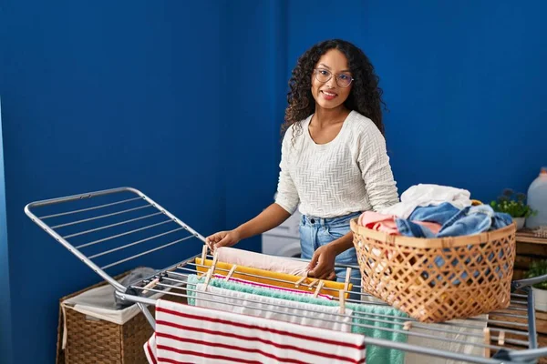 Genç Latin kadın gülümsüyor çamaşırhanede kendine güveni tam çamaşır ipine asılan kıyafetler.