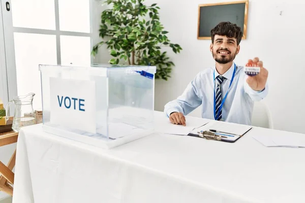 Young hispanic politic party worker man holding i voted badge at electoral college.