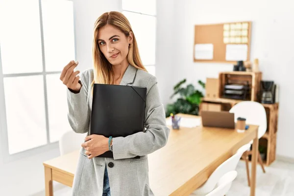 Blonde business woman at the office doing money gesture with hands, asking for salary payment, millionaire business