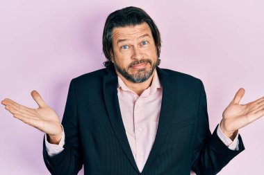 Orta yaşlı beyaz bir adam iş kıyafetlerinden bihaber ve kolları açık, hiçbir fikri yok ve şüpheli bir yüzü var.. 