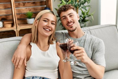 Genç beyaz çift gülümsüyor. Kırmızı şarapla kadeh kaldırıyorlar..