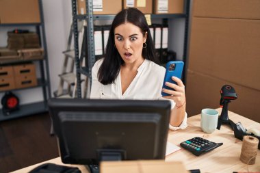 Küçük işletme şirketinde çalışan genç İspanyol kadın akıllı telefonuyla korkmuş ve şaşırmış bir şekilde ağzı açık kalmış, inançsız bir yüz. 