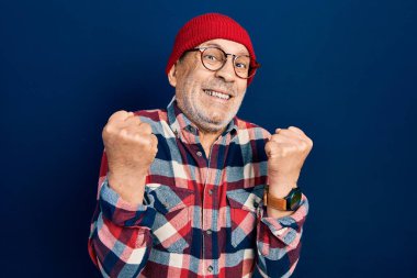 Yakışıklı, hippi görünümlü, yün şapkalı, çok mutlu ve heyecanlı kolları havada, gülümseyen ve başarı için bağıran, kazanan jestler yapan olgun bir adam. kutlama konsepti. 