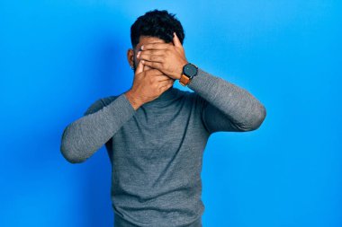 Balıkçı yaka kazak giyen sakallı Arap adam gözlerini ve ağzını elleriyle kapatıyor, şaşırmış ve şok olmuş. duygu gizleme 