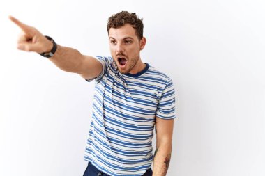 Yakışıklı genç adam izole edilmiş arka planda duruyor. Parmağıyla işaret ediyor. İleride şaşırmış, ağzı açık. 