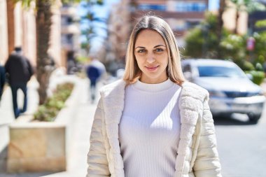 Kendine güvenen genç bir kadın caddede kollarını kavuşturmuş duruyor.