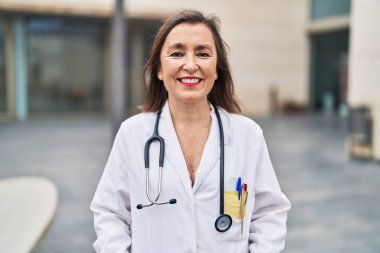 Orta yaşlı kadın doktor üniforması giyiyor. Gülümsüyor.