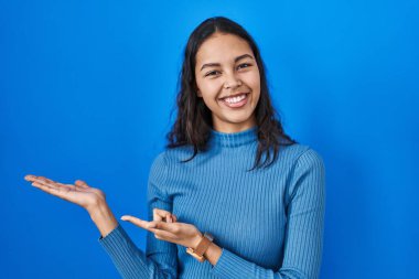 Mavi arka plan üzerinde duran genç Brezilyalı kadın hayrete düşmüş ve kameraya gülümserken eliyle ve parmağıyla işaret ediyordu.. 