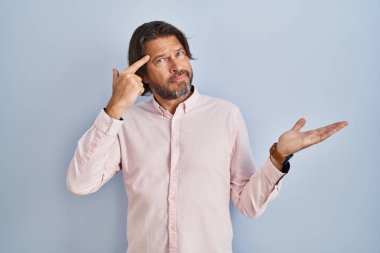 Zarif tişört giyen yakışıklı orta yaşlı bir adam. Avuç içinin açık olması, fotokopi alanını göstermesi ve alnını işaret etmesi kafasını karıştırmış ve rahatsız etmiş. Bunu bir düşün.. 