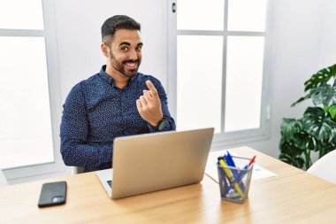 Ofiste sakallı, laptopla çalışan genç İspanyol bir adam seni buraya davet ediyor. Elinle mutlu bir karşılama ve gülümsemeyle gel. 